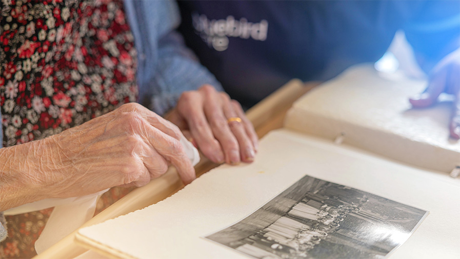 A Bluebird Care customer reminisces by looking through an old photo album with a care professional