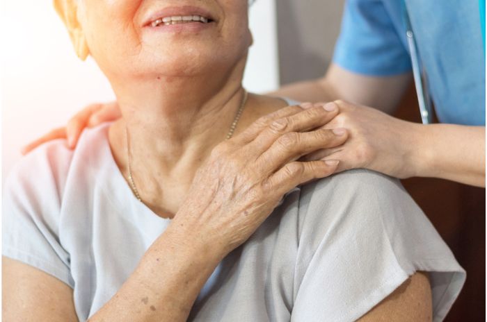 A care worker places a reassuring hand on an older lady's shoulder