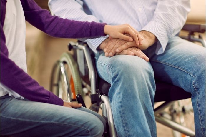 A carer puts their hand reassuringly on the lap of someone in a wheelchair