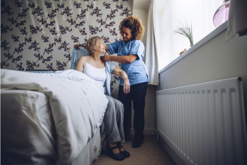 A carer helps an elderly lady dress in her bedroom