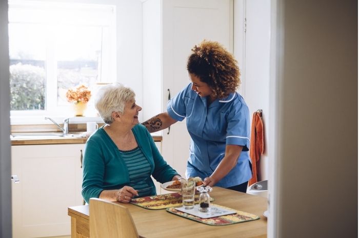 A carer brings an elderly woman some food