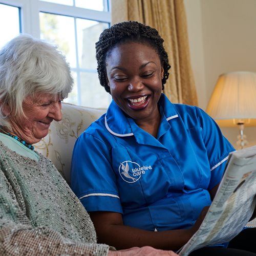 A Bluebird Care live-in care assistant showing a happy customer a newspaper