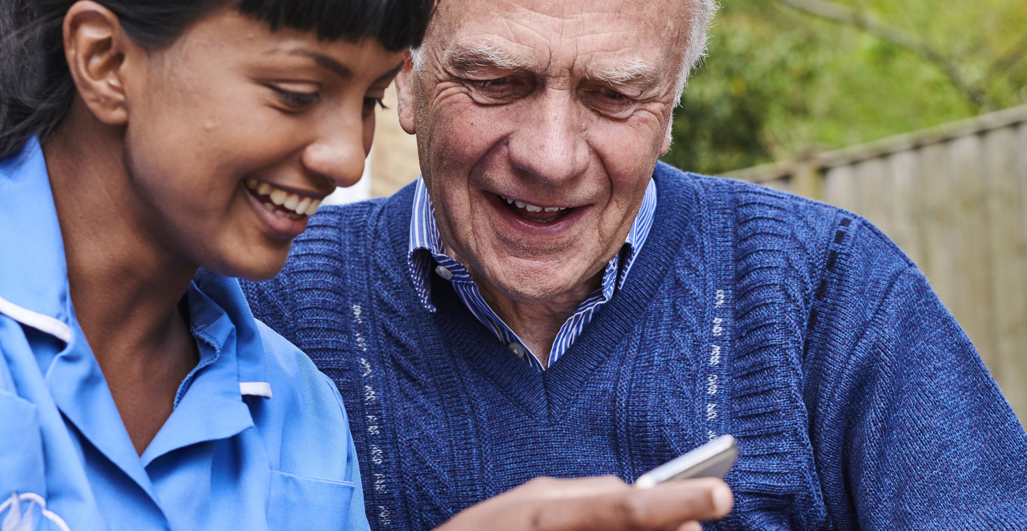 Blue Bird Care assistant showing elderly man her mobile phone